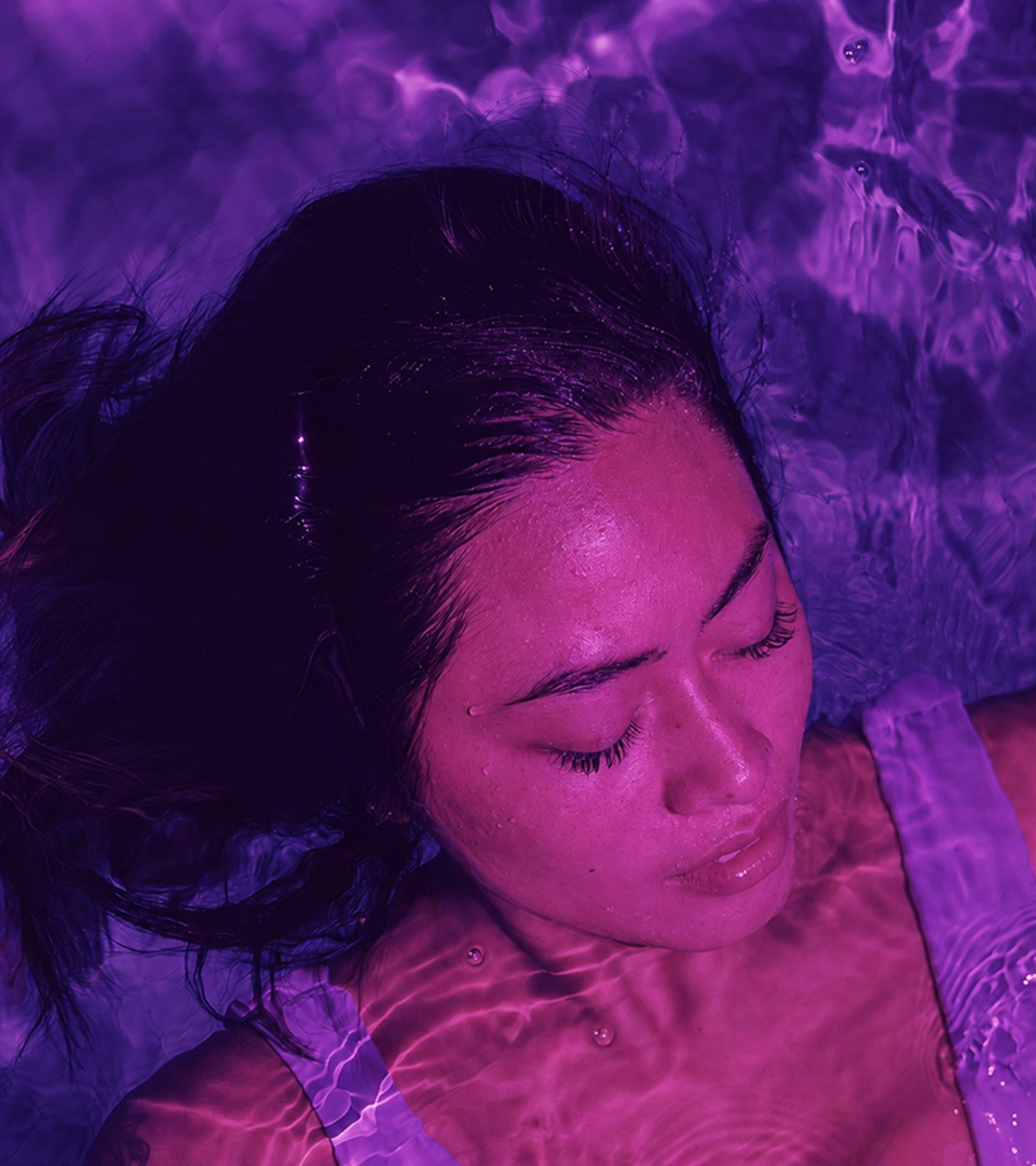 Visage et épaules d'une femme flottant dans le bassin de flottaison avec un dégradé de couleur violet apaisant